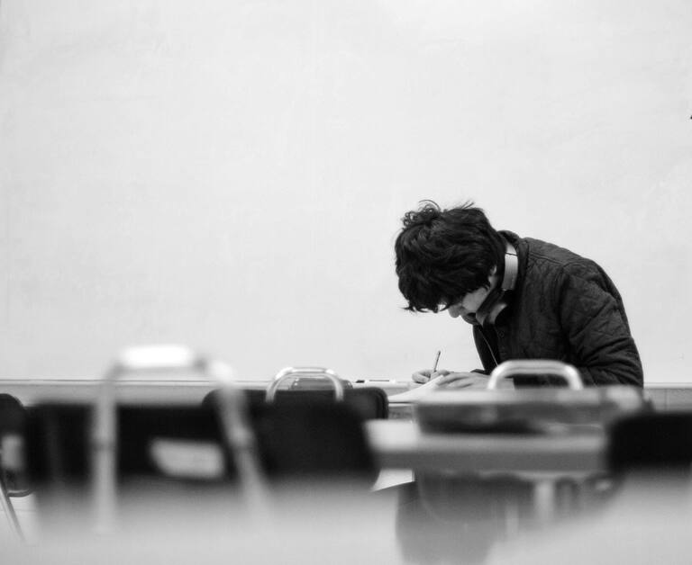 Young man in school setting, writing notes on piece of paper